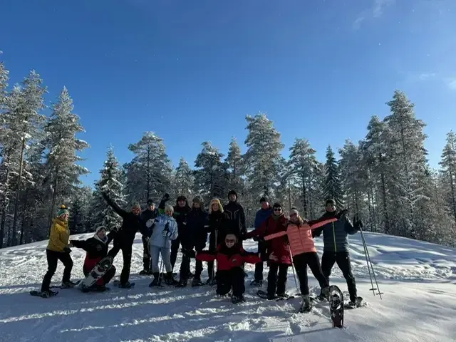 Die Reisegruppe posiert bei strahlendem Sonnenschein mit Schneeschuhen im Winterwald