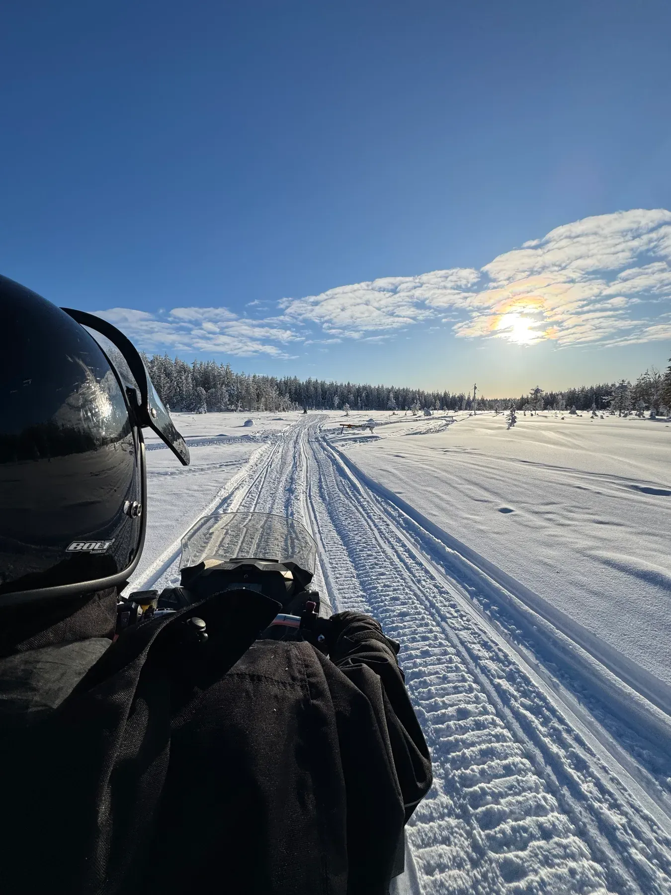 Blick über den Lenker eines Motorschlittens auf eine sonnige Schneepiste